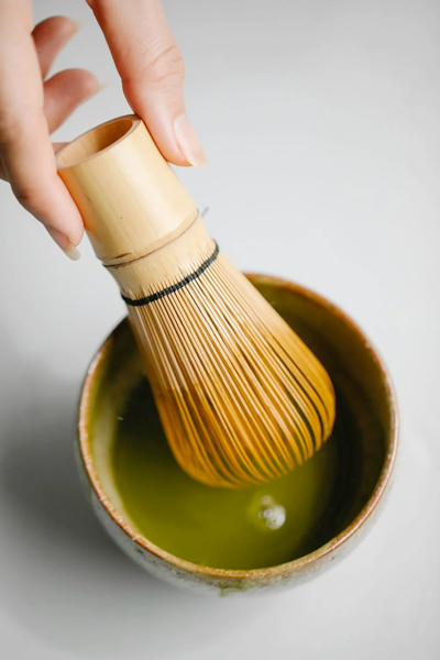 Traditionelle Matcha-Zubereitung mit einem Bambus-Chasen-Besen in einer Keramik-Chawan-Schale, Schritt für Schritt gezeigt für die perfekte schaumige Konsistenz
